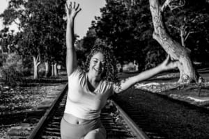 A woman smiles while doing a yoga pose on the railroad tracks.