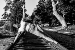 A young woman doing a dedicated yoga pose on the railroad tracks.