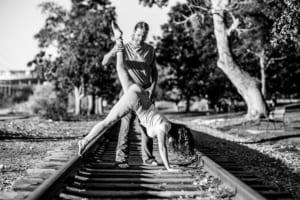 A man teaching yoga to a woman on the railroad tracks.